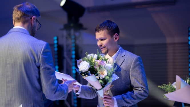 Vīrietim tiek pasniegts apbalvojums un ziedi