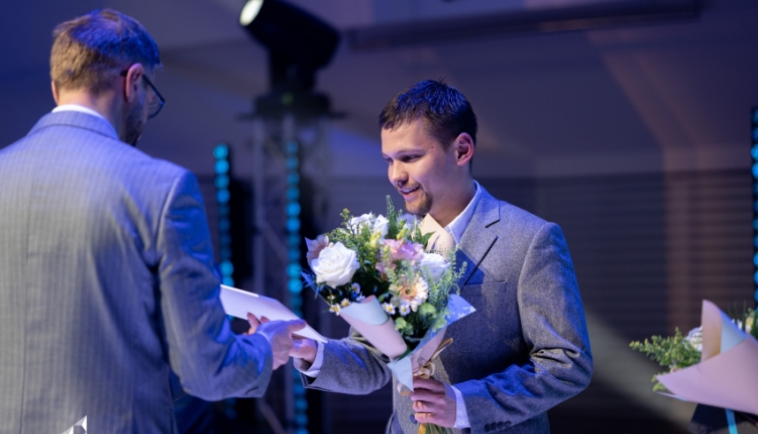 Vīrietim tiek pasniegts apbalvojums un ziedi